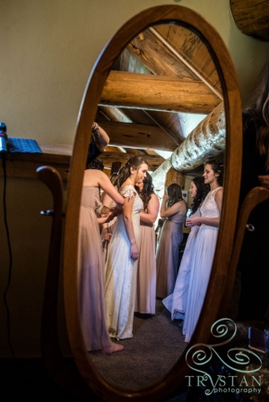 A shot of the bride in the mirror as her mom and bridesmaids get her dress on.