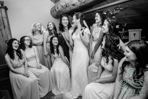 A bride standing in the middle of her bridesmaids and laughing.