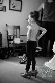A flower girl standing in the brides shoes as she watches the bride get ready before a wedding.