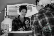 A bride smiling at herself in the mirror as she does her own makeup before the wedding.