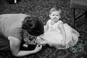A tiny flower girl sits crying while she gets her shoes put on before the wedding.