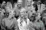 A bride smiling at all her bridesmaids around her as they sit in their floral bridal robes before the wedding.