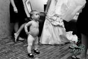 A little baby flower girl fixing her tights as she watches a bride get into her dress before the wedding.