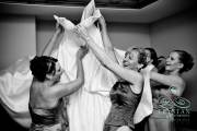 A bride's mom and the bridesmaids laughing as they struggle to get the bride's dress on her before the wedding.