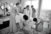 A bride laughing as her bridesmaids put the garter on her leg before the wedding.