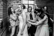 A bride surrounded by her bridesmaids as they try to fasten her corset before the wedding.