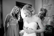 A bride laughing as her mother and sister work on lacing up the back of her dress before the wedding.