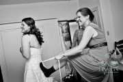 A funny photograph of a bridemaid putting her foot on the bride's back to pull on the corset ribbons before the wedding.