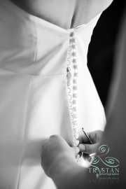 A mother's hands work diligently she tries to fasten tiny hooks on the back of a bride's dress before the wedding.