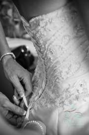 A photograph of hands holding a button-hook tool as they fasten the back of the dress before the wedding.