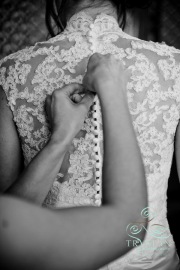 A bridesmaid's hands are carefully buttoning up the lace back of a bride's dress before the wedding.