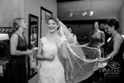 A photograph of a bride laughing as her bridesmaids fan the veil out behind her before the wedding.