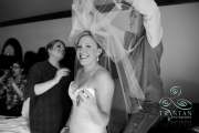 A bride smiling as the makeup artist and her mother try to work out how to attach the veil to her hair.