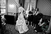 Bridesmaids clap and fawn over the bride as she stands ready in her wedding dress.