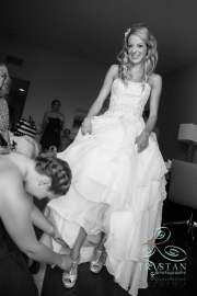 A bridesmaid bends low to help the bride put her shoes on.
