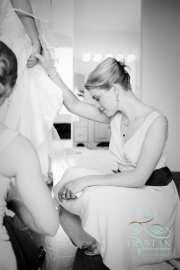 A lovely bridesmaid quietly holds the bride's hand as she balances herself as her shoes are put on.
