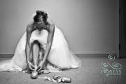A bride who is a ballerina sits against the wall as she puts on her ballerina slippers under her wedding dress.