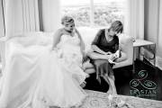 A bride laughing as she rests her foot on her mother's leg as her mother puts her heels on.