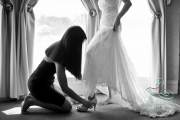 A bride stepping into her shoes as her bridesmaid kneels and help slide the heels on.