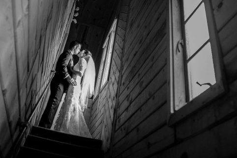 A bride and groom kissing in a dramatically lit stairwell.