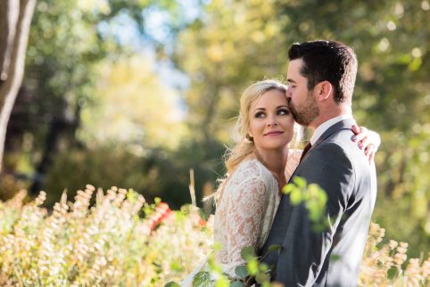 A bride and groom cuddling in in a garden in the warm Colorado sunlight on their wedding day.