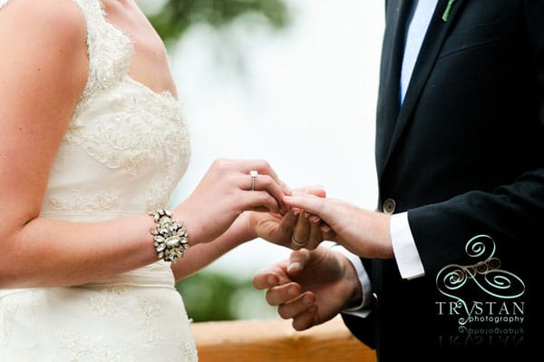 A photograph of a bride's hands as she places the wedding ring on the groom's hand during a wedding ceremony.