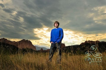 A portrait of a young male high school senior standing confidently in a field with The Garden of the Gods and stunning sunset skies behind him.