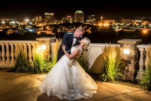 A bride and groom dipping on the balcony at night with the Pinery's view of downtown Colorado Springs behind them.