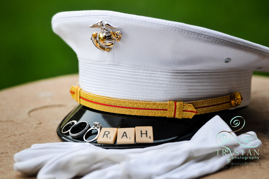 A photograph of a Marine's cover with the wedding rings and scrabble tiles on the brim that spell "Ooorah".