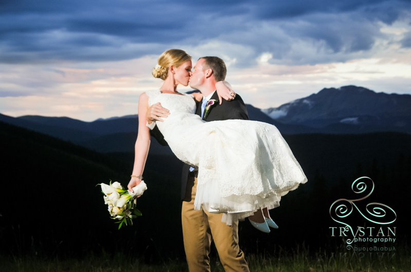 A photograph of a bride being carried in the arms of a groom at dusk on top of Keystone at TImber Ridge with the mountains behind them.