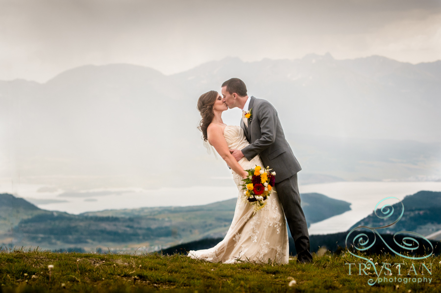 A wedding photograph of a bride and groom kissing at the top of Keystone mountain with Lake Dillon behind.