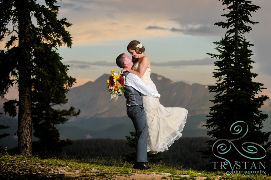 A wedding photograph of a bride being lifted in the arms of a groom at sunset on top of Keystone Resort at Timber Ridge.